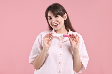 Photo of Happy young woman with pregnancy test on pink background