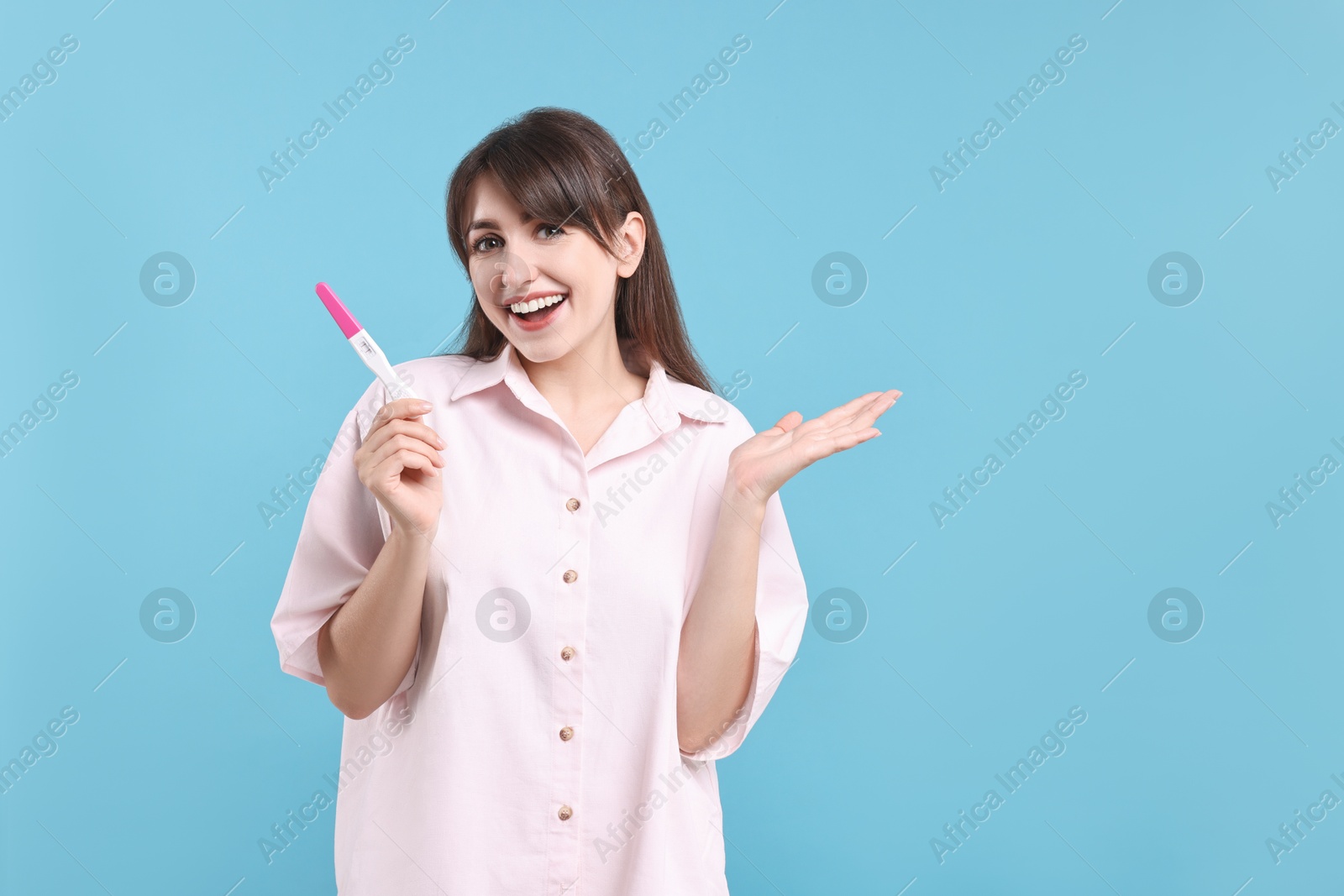 Photo of Happy young woman with pregnancy test on light blue background, space for text