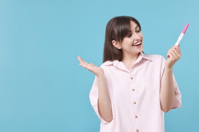 Happy young woman with pregnancy test on light blue background, space for text