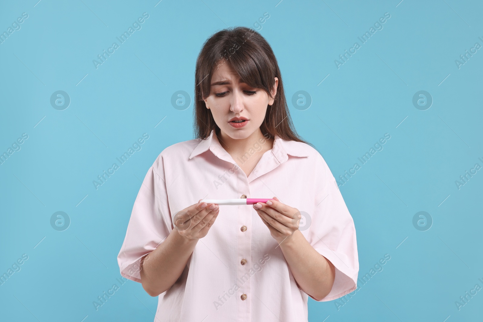 Photo of Worried young woman with pregnancy test on light blue background