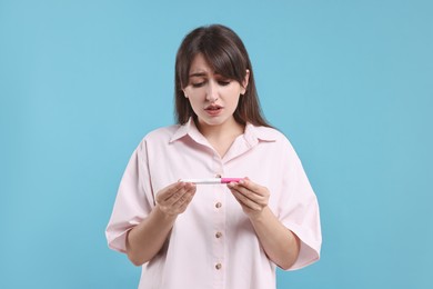 Worried young woman with pregnancy test on light blue background