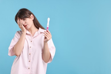 Photo of Worried young woman with pregnancy test on light blue background, space for text