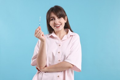 Photo of Happy young woman with pregnancy test on light blue background