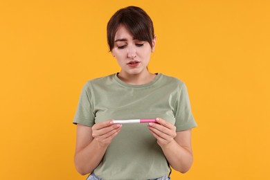 Worried young woman with pregnancy test on orange background