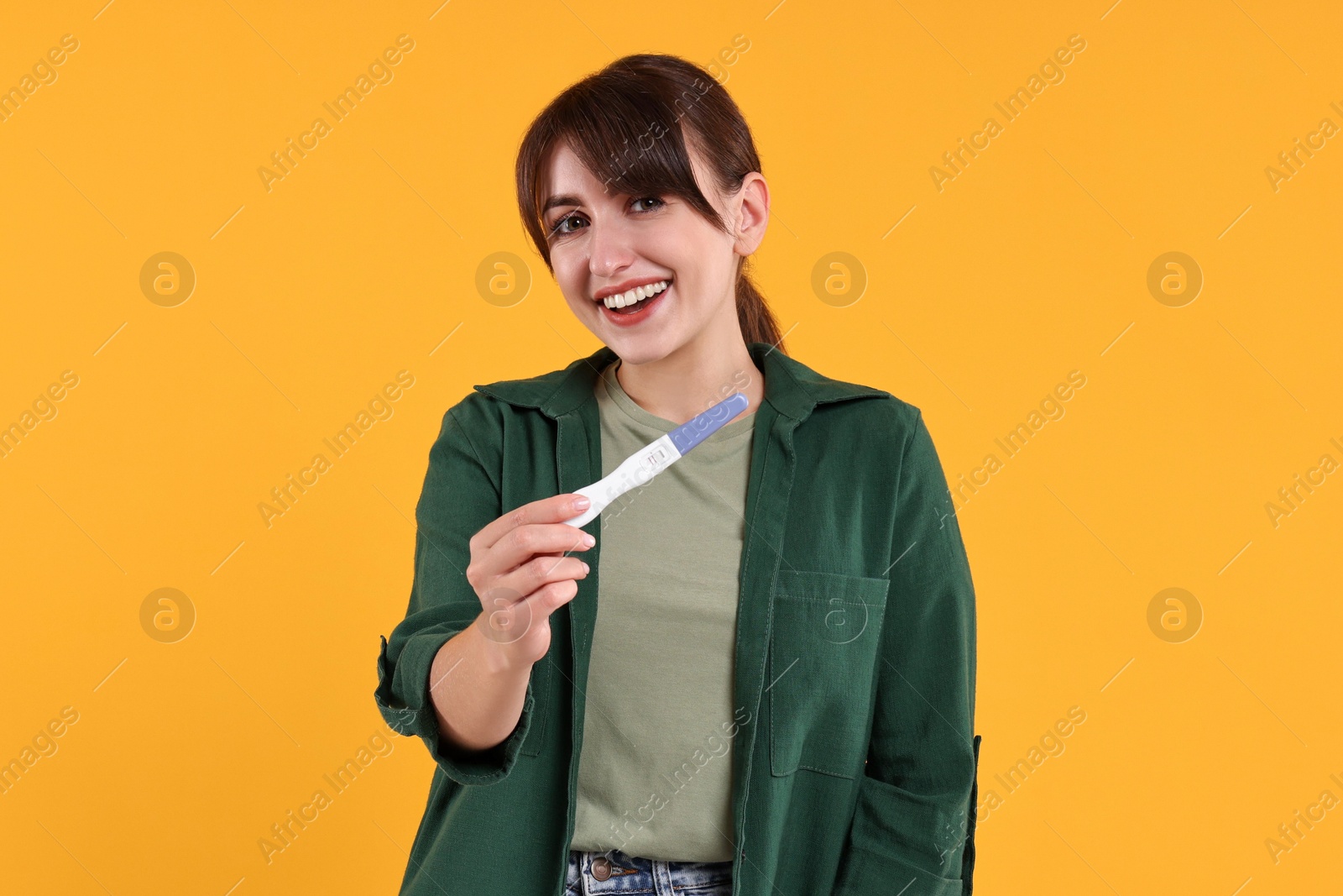 Photo of Happy young woman with pregnancy test on orange background