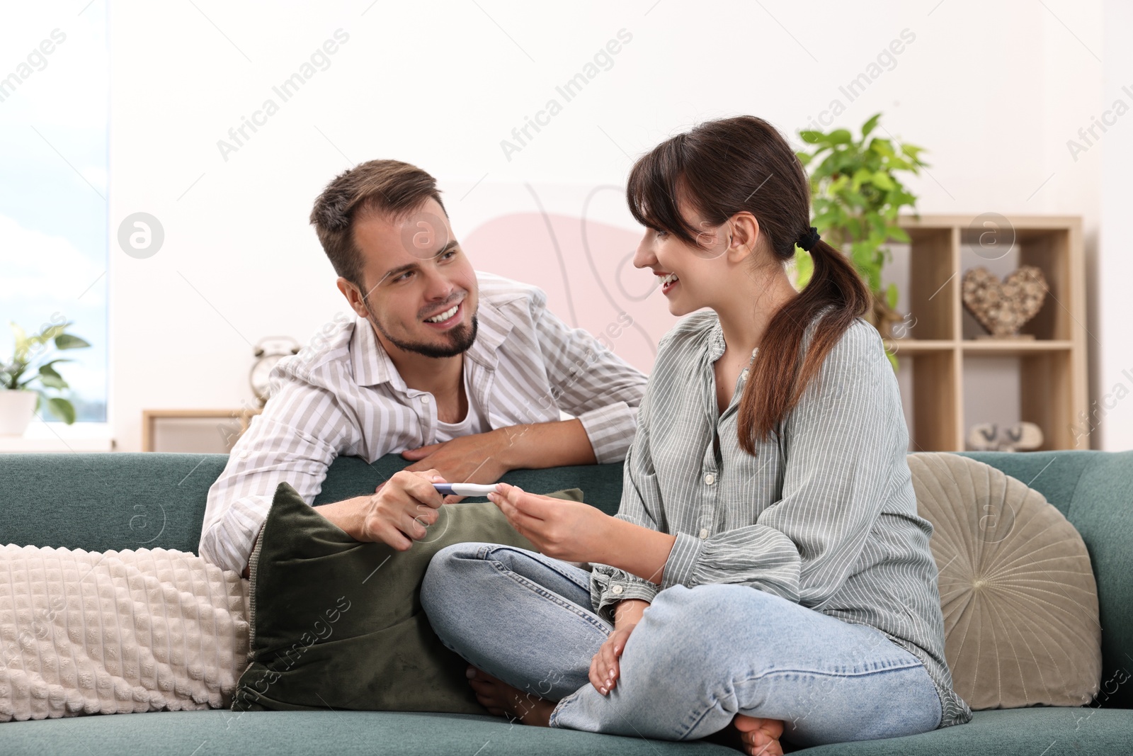 Photo of Happy young couple with pregnancy test on sofa at home