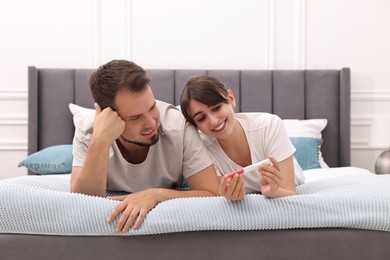 Happy young couple with pregnancy test on bed at home