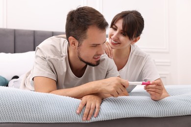 Happy young couple with pregnancy test on bed at home