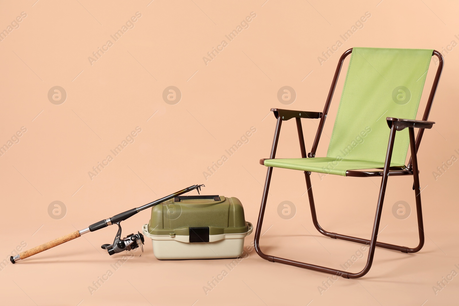 Photo of Folding chair, fishing rod and tackle box on beige background