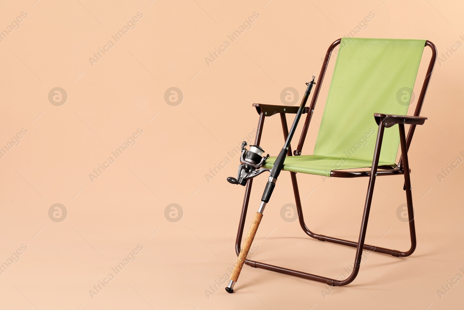 Photo of Folding chair and fishing rod on beige background, space for text