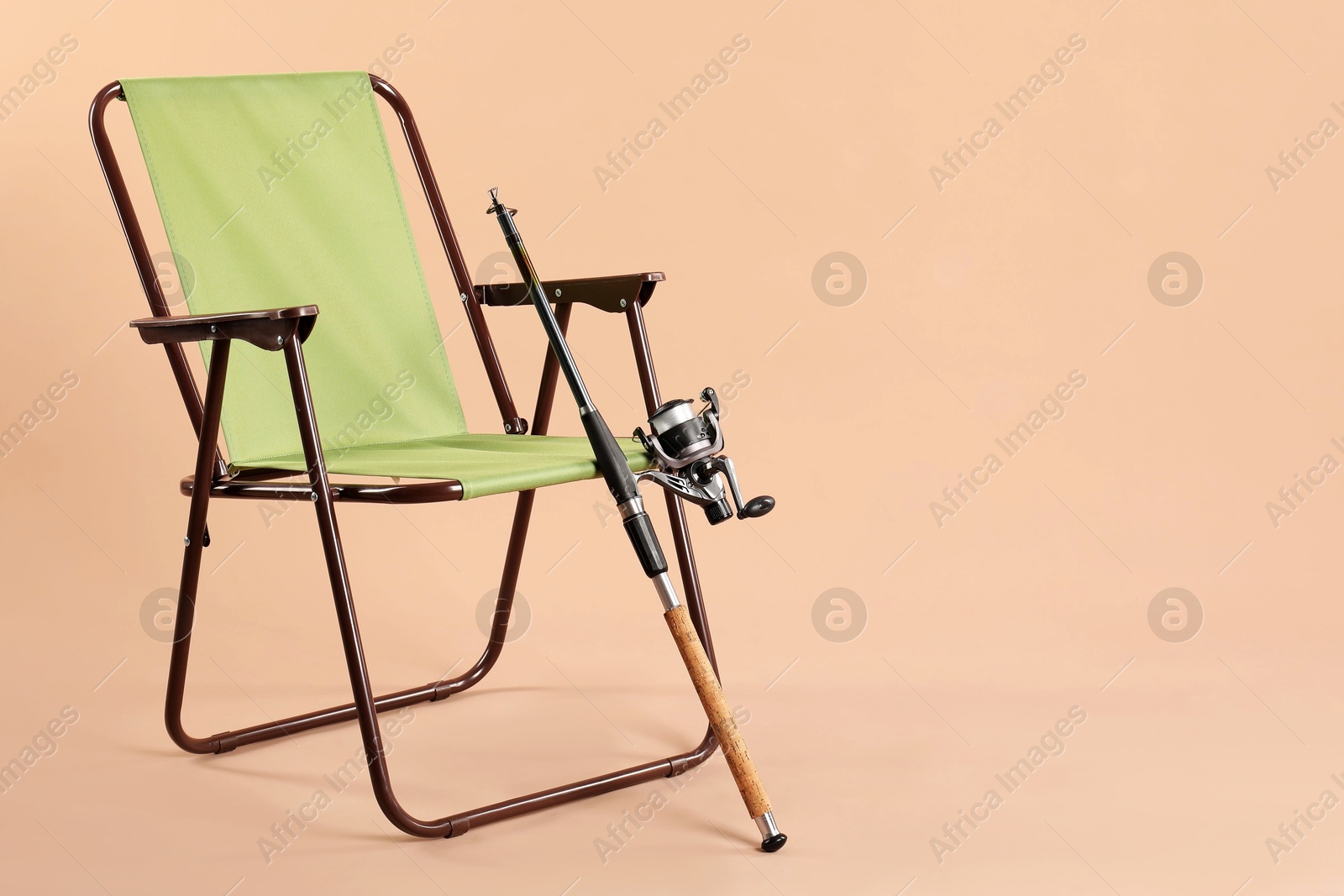 Photo of Folding chair and fishing rod on beige background, space for text