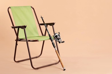 Photo of Folding chair and fishing rod on beige background, space for text