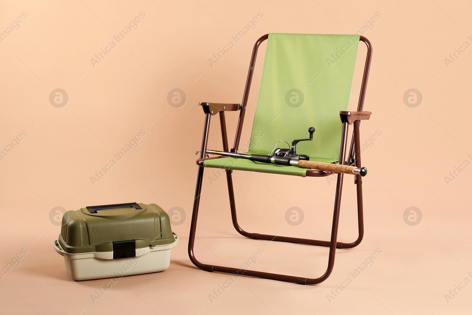 Photo of Folding chair, fishing rod and tackle box on beige background