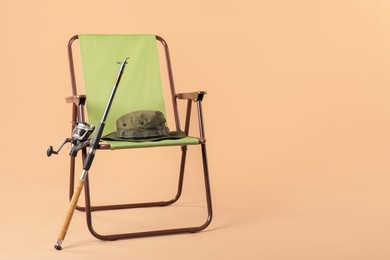 Photo of Folding chair, fishing rod and hat on beige background, space for text