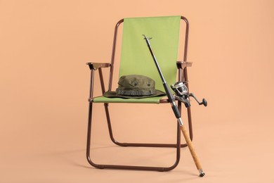 Photo of Folding chair, fishing rod and hat on beige background