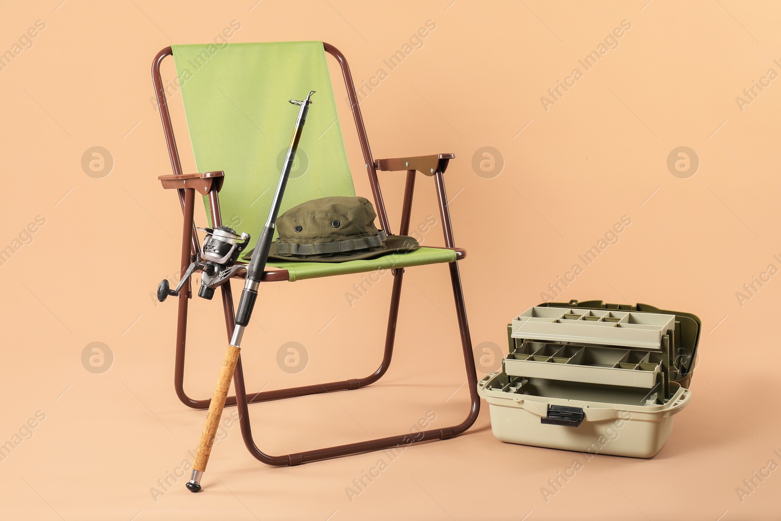 Photo of Folding chair, fishing rod, hat and tackle box on beige background