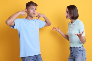 Emotional young couple arguing on orange background