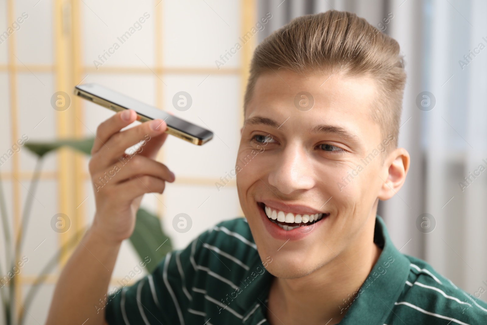 Photo of Young man with smartphone listening to voice message at home