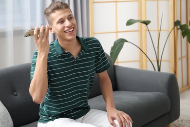 Young man with smartphone listening to voice message at home