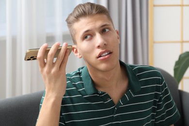 Young man with smartphone listening to voice message at home