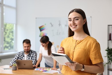 Happy young designer with notebook in office