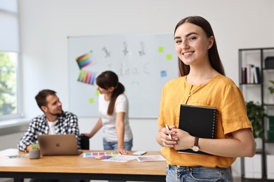 Happy young designer with notebook in office