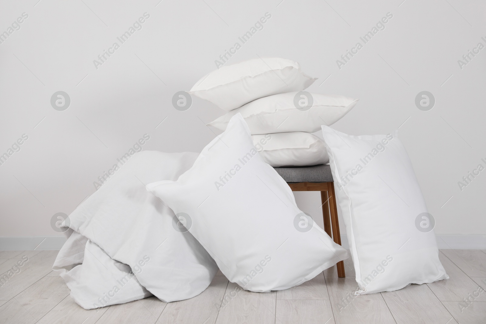 Photo of Clean pillows, blanket and stool on floor near white wall