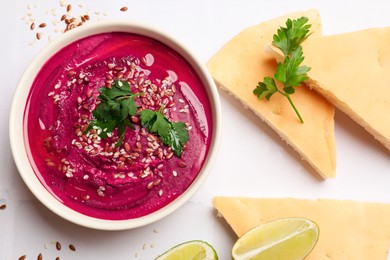 Tasty beetroot hummus in bowl and products on white table, flat lay