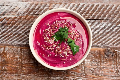 Tasty beetroot hummus, parsley and seeds in bowl on wooden table, top view