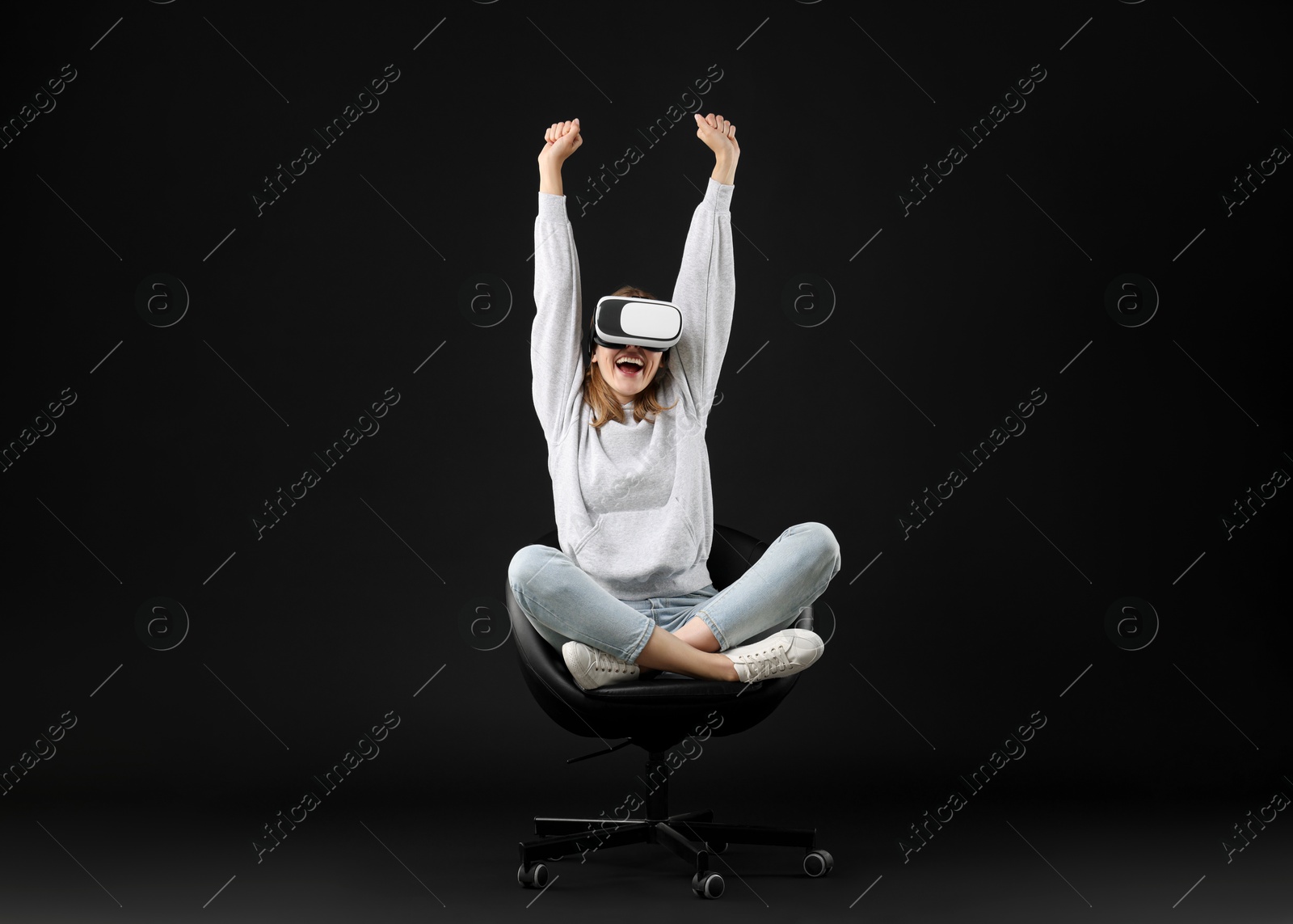 Photo of Happy woman with virtual reality headset sitting on chair against black background