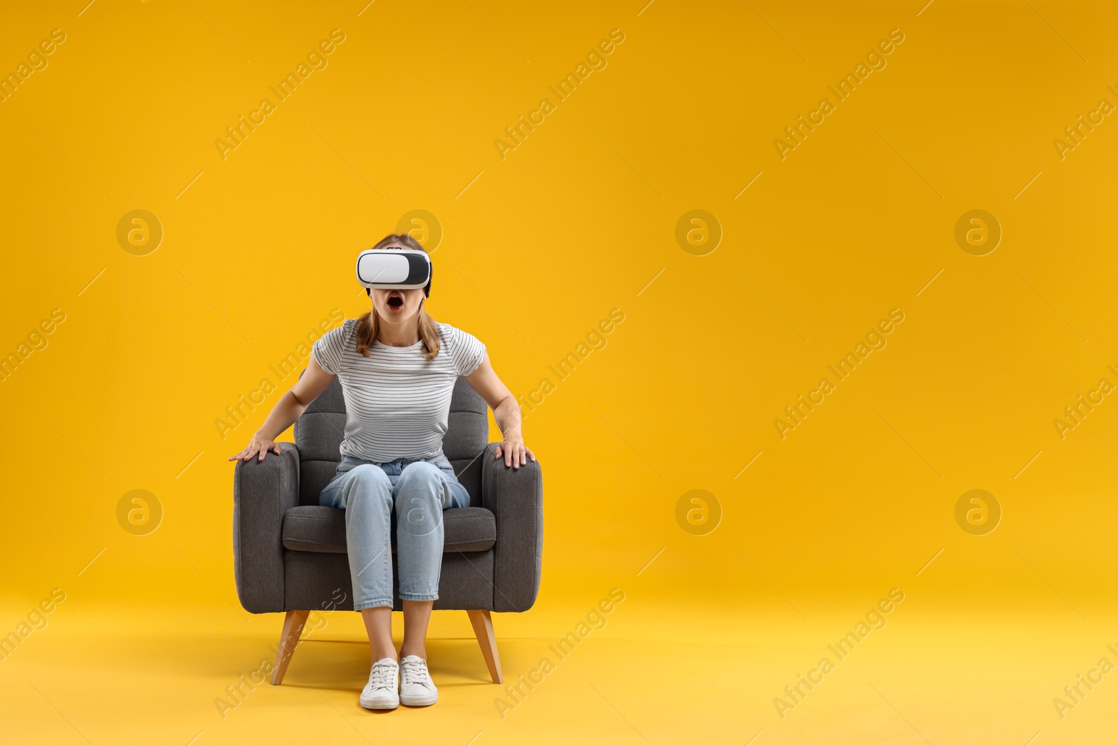 Photo of Emotional woman with virtual reality headset sitting in armchair on yellow background, space for text