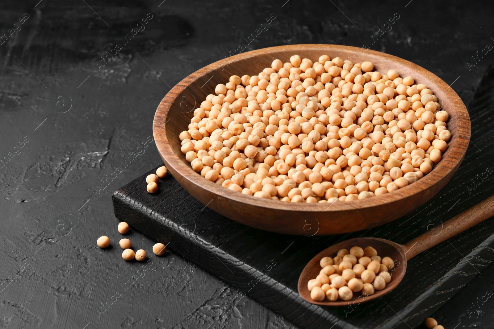 Photo of Dried peas in bowl and spoon on dark textured table, closeup