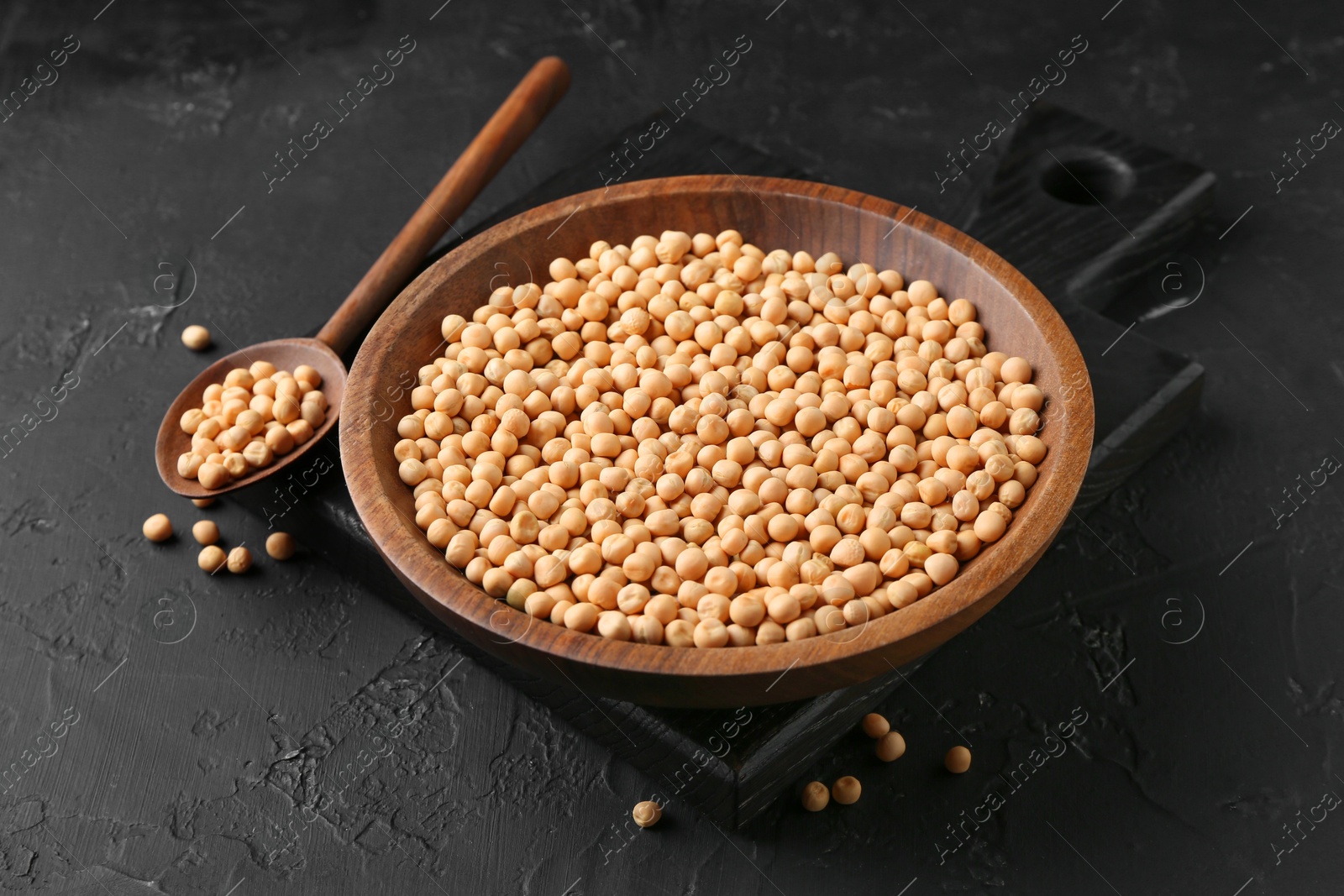 Photo of Dried peas in bowl and spoon on dark textured table, closeup