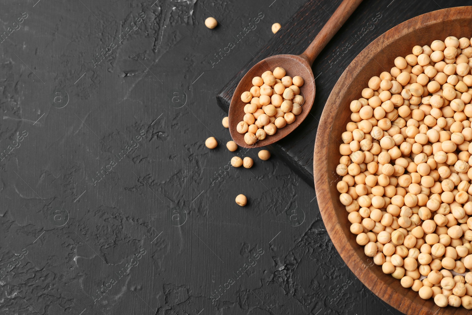 Photo of Dried peas in bowl and spoon on dark textured table, top view. Space for text