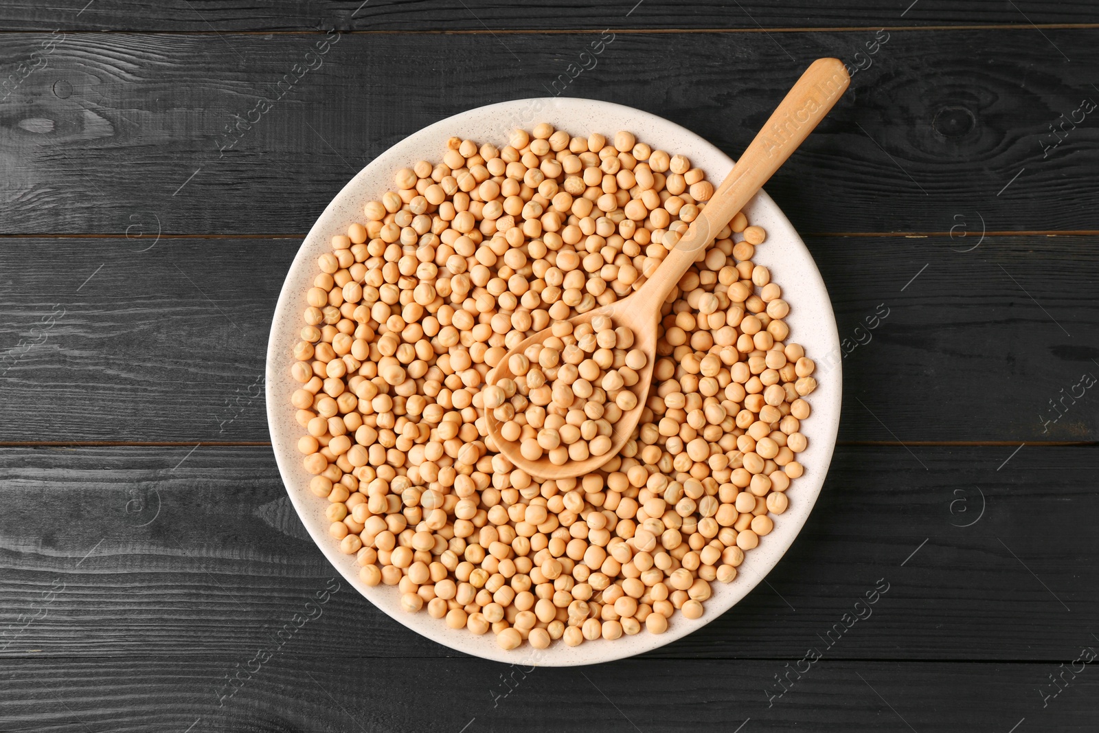 Photo of Dried peas in bowl and spoon on black wooden table, top view