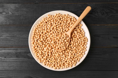 Dried peas in bowl and spoon on black wooden table, top view