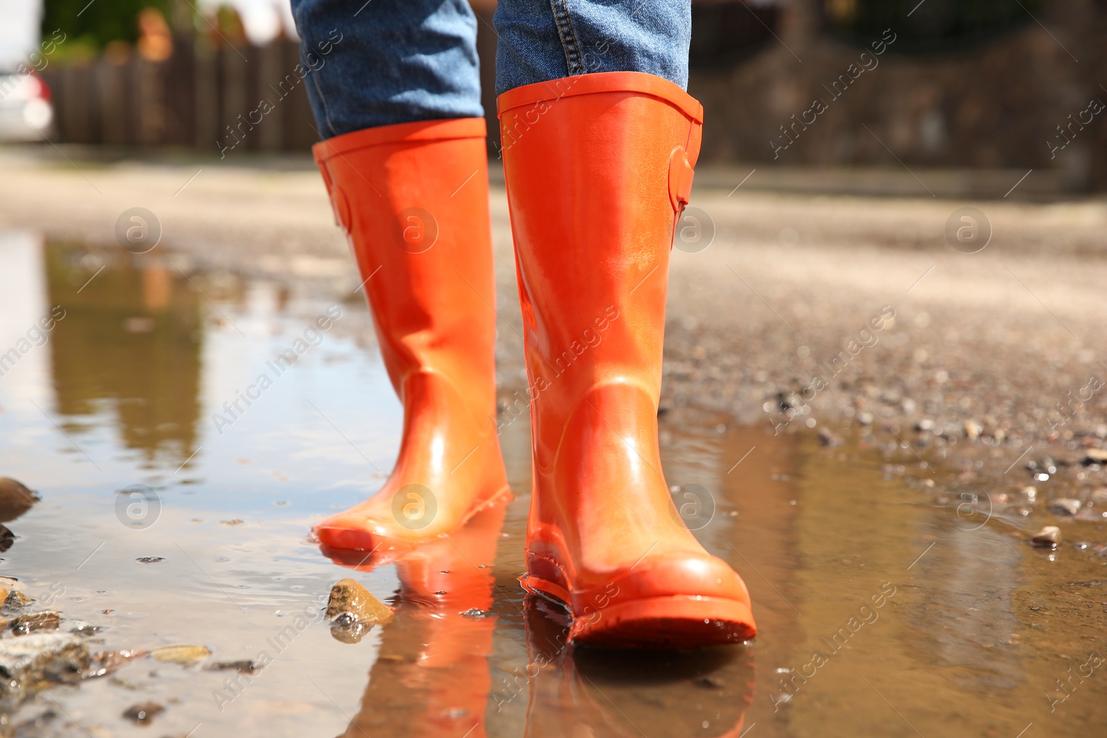 Photo of Woman wearing orange rubber boots standing in puddle outdoors, closeup