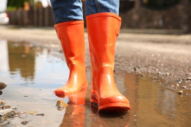 Woman wearing orange rubber boots standing in puddle outdoors, closeup