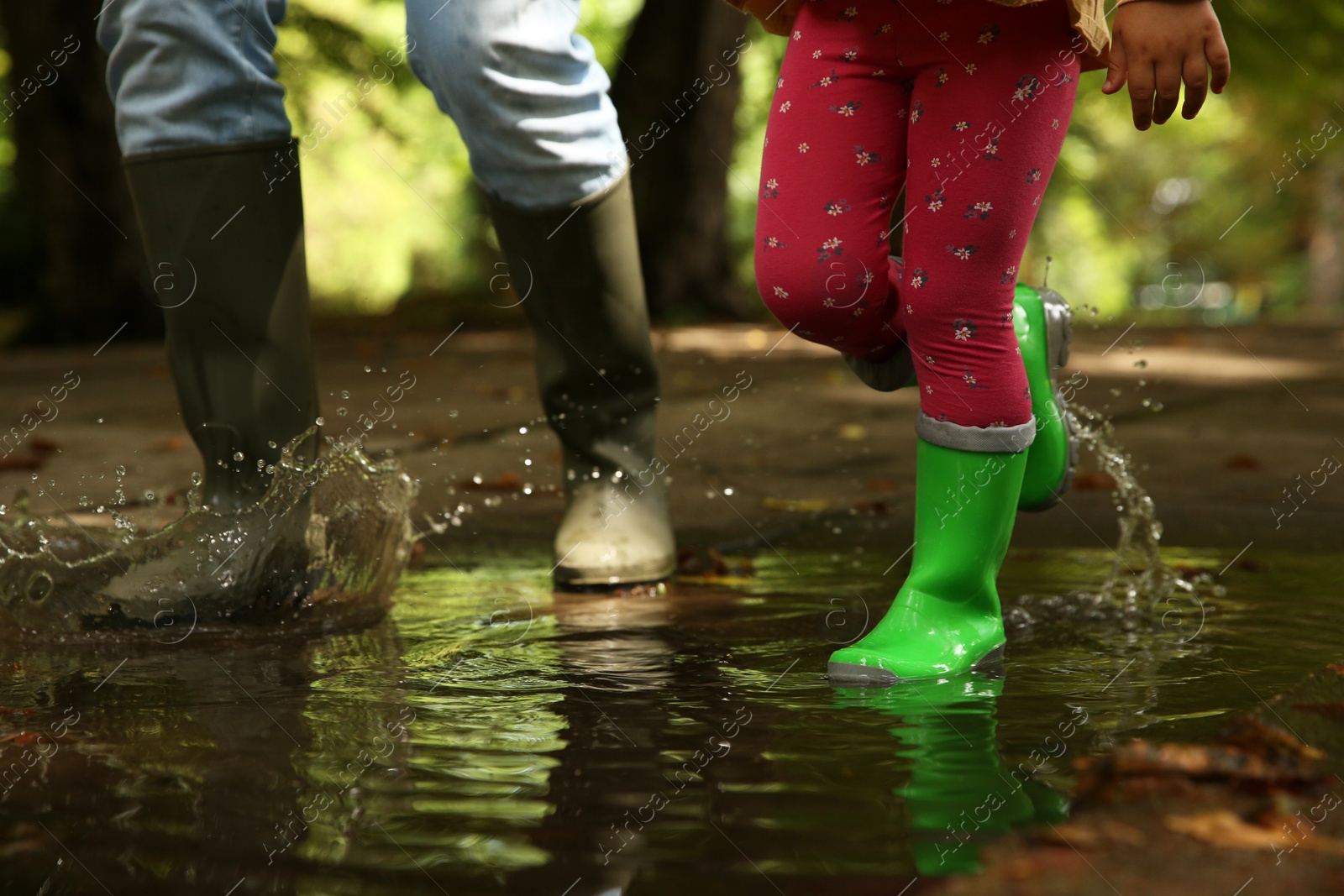 Photo of Mother and daughter wearing rubber boots walking in puddle outdoors, closeup