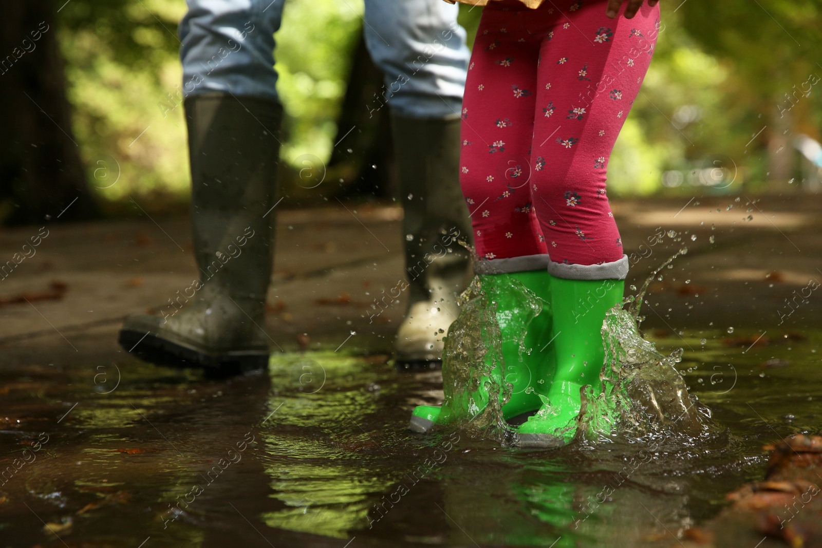 Photo of Mother and daughter wearing rubber boots standing in puddle outdoors, closeup