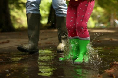 Photo of Mother and daughter wearing rubber boots standing in puddle outdoors, closeup