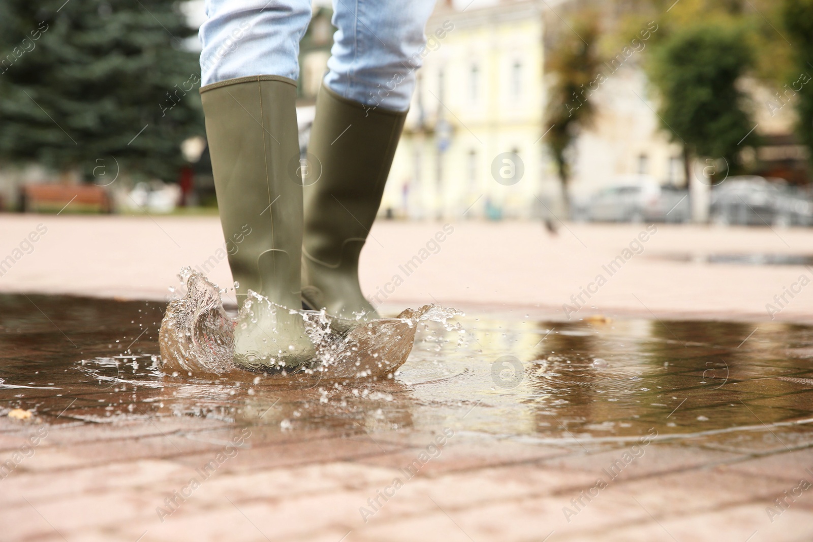 Photo of Woman wearing rubber boots walking in puddle outdoors, closeup. Space for text