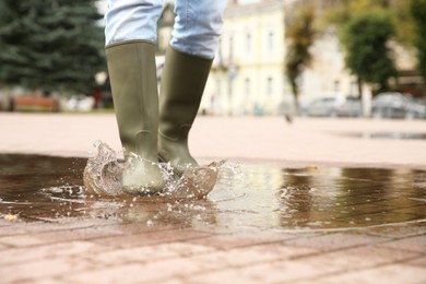 Woman wearing rubber boots walking in puddle outdoors, closeup. Space for text