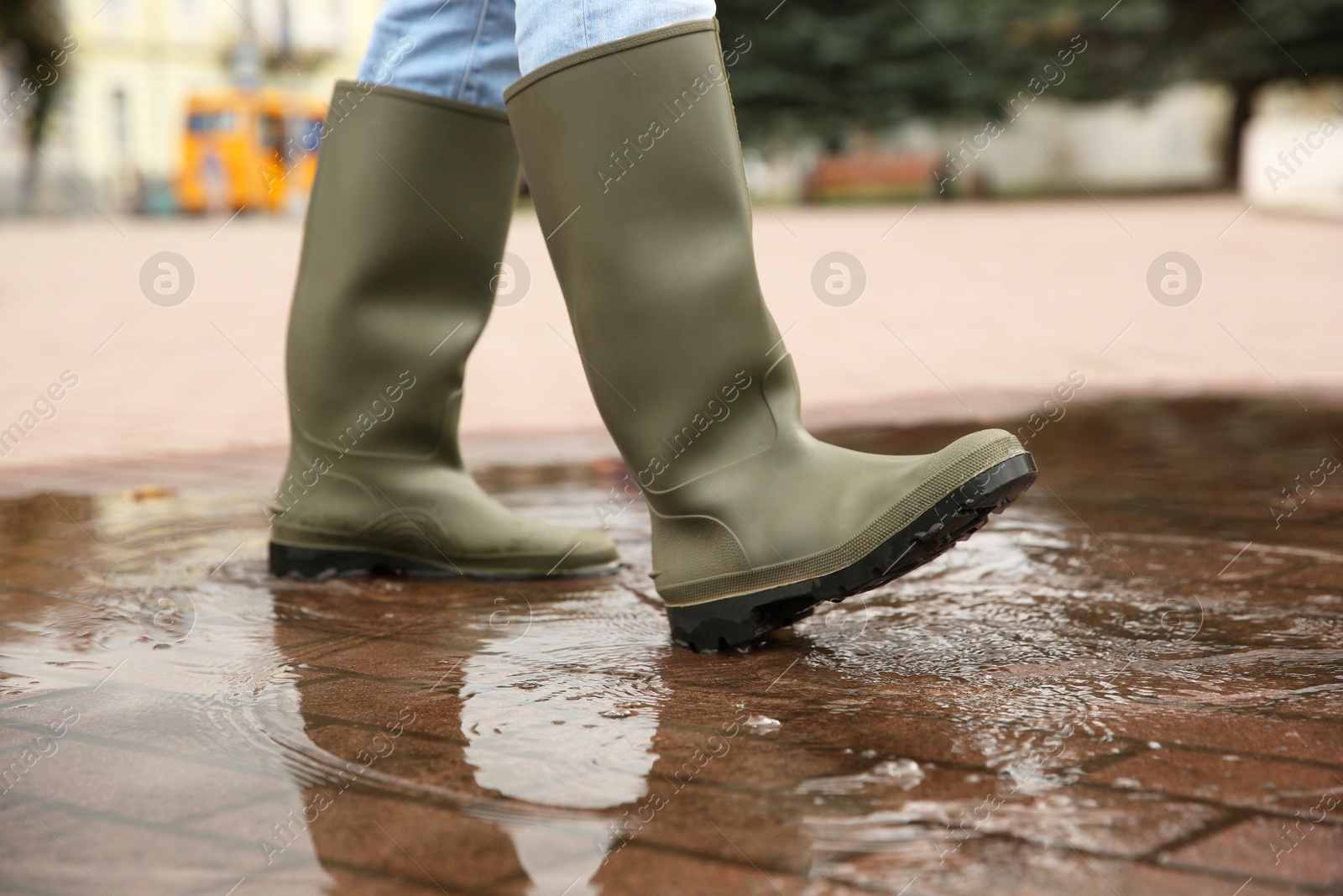 Photo of Woman wearing rubber boots walking in puddle outdoors, closeup