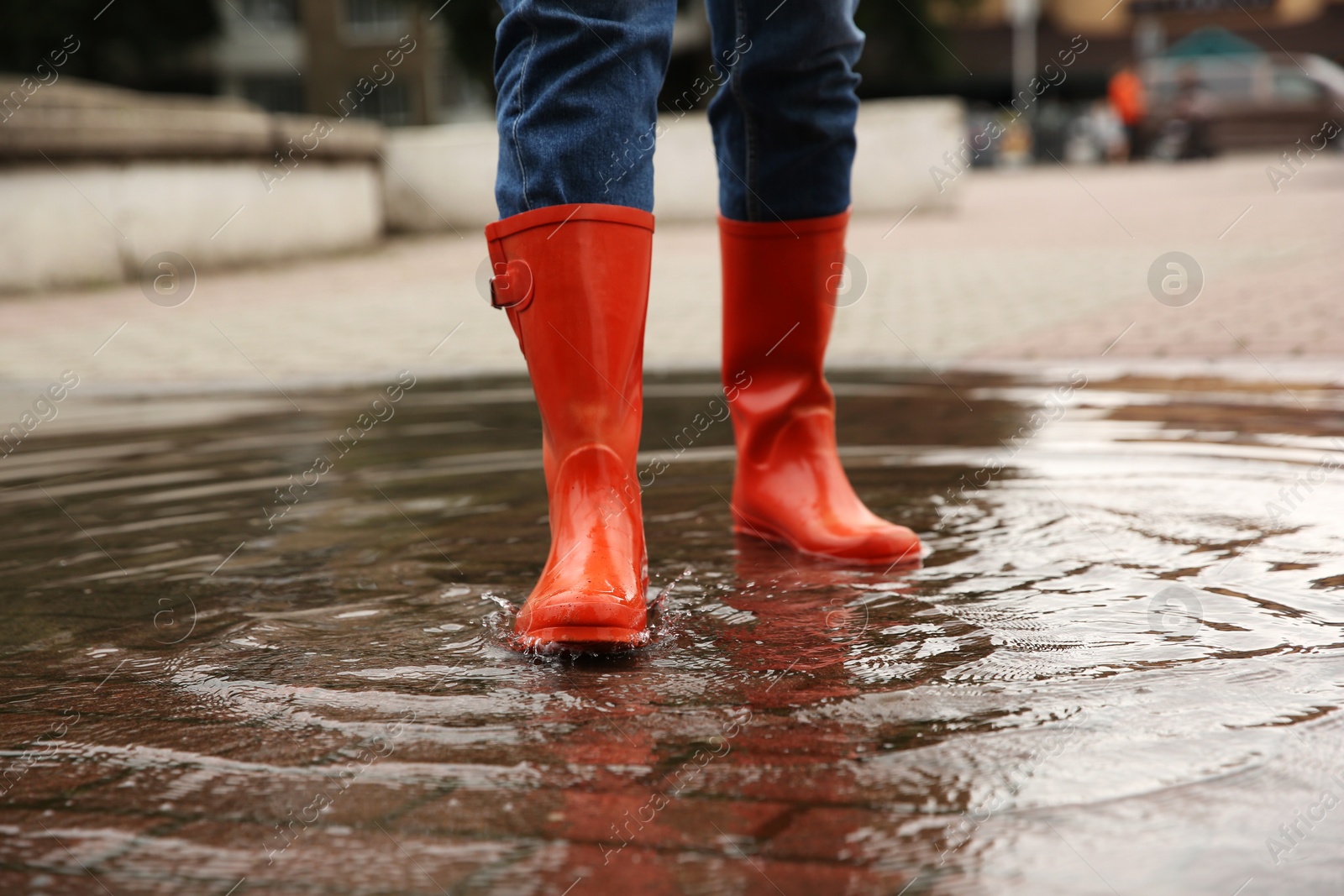 Photo of Woman wearing orange rubber boots standing in puddle outdoors, closeup