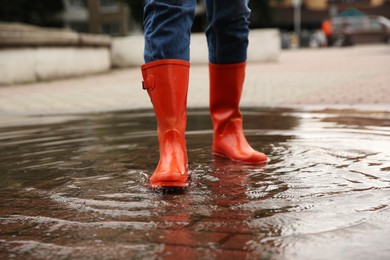 Photo of Woman wearing orange rubber boots standing in puddle outdoors, closeup