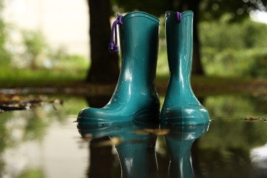 Pair of colorful rubber boots in puddle outdoors