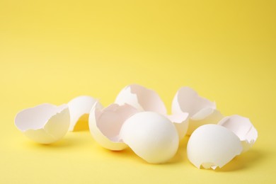 Photo of Pile of broken eggshells on yellow background, closeup