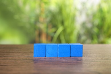 Photo of Many blank colorful cubes on wooden table outdoors