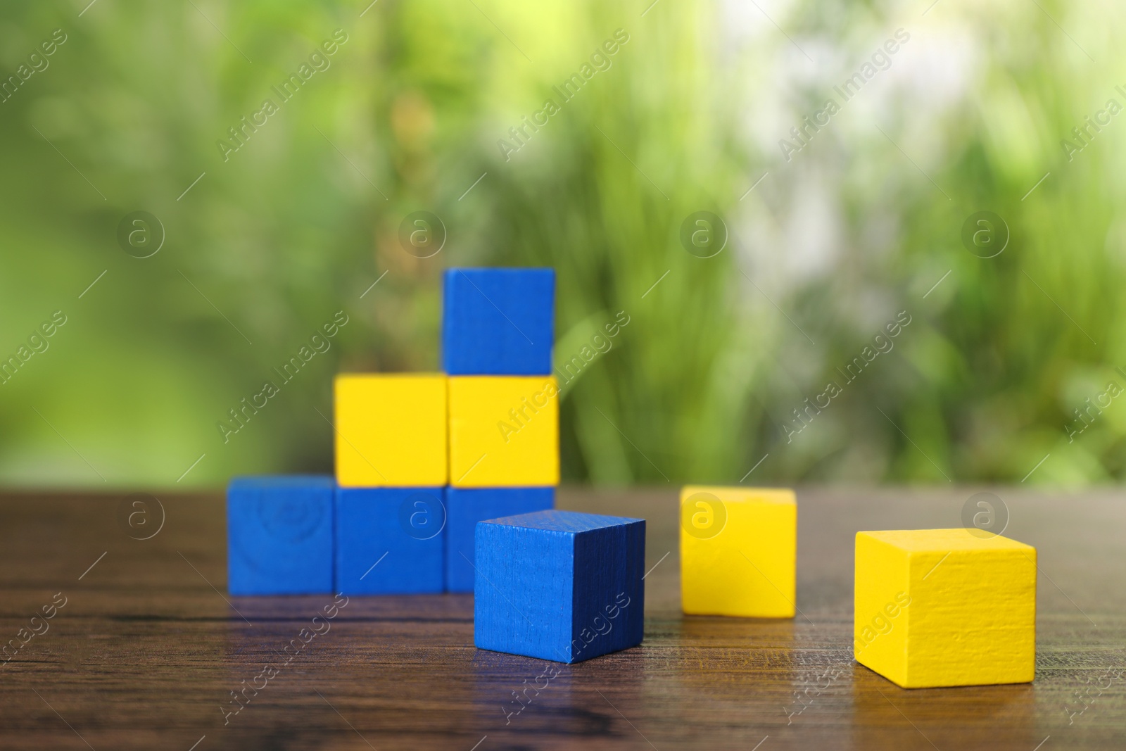 Photo of Many blank colorful cubes on wooden table outdoors